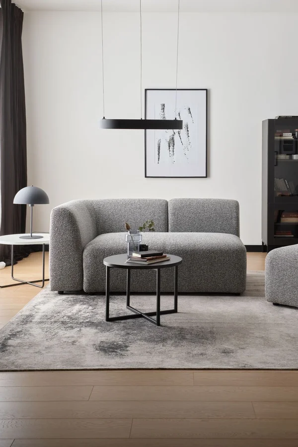 Nowoczesna szara sofa w minimalistycznym wnętrzu z czarnymi akcentami.